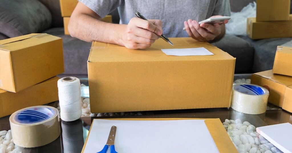 A man sits at a table with packing boxes and a pen, preparing supplies for packing dishes.