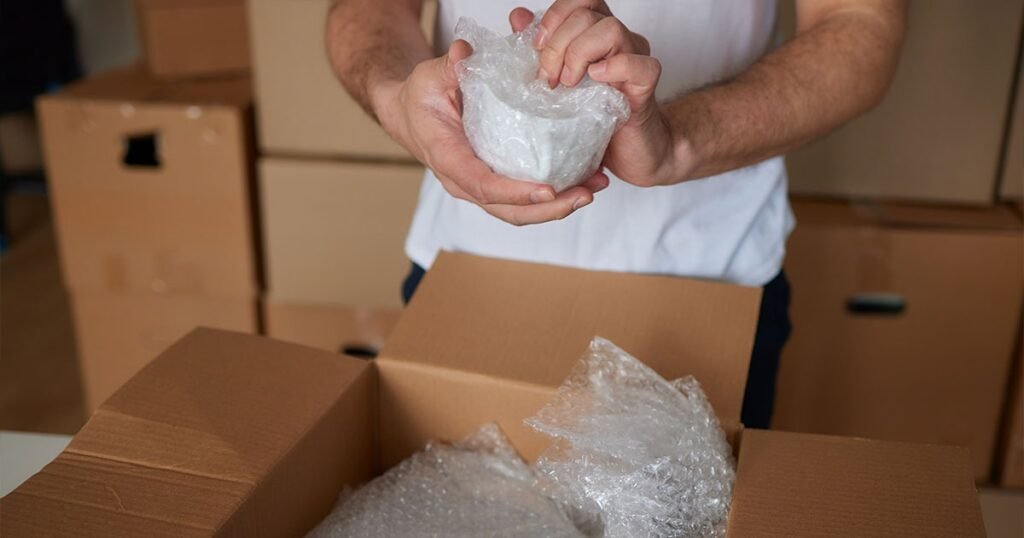 A man holds a package of bubble wrap, demonstrating a step in the process of packing dishes for moving.