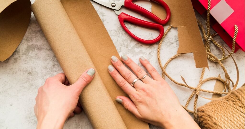 Woman's hands holding scissors and wrapping paper, preparing to package books with essential packing materials.