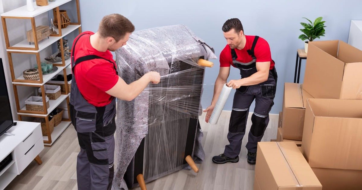 Two men in red shirts and black pants moving a large piece of furniture, part of a furniture inventory before moving.