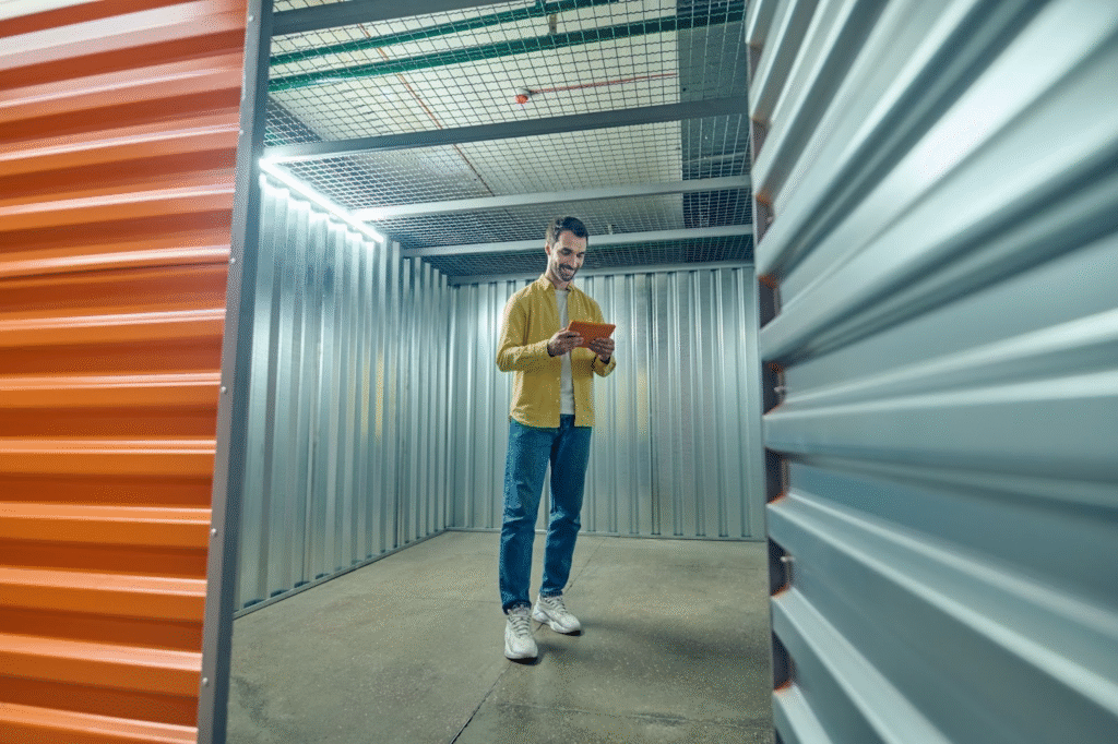 A man stands inside an empty 10×10 storage unit, smiling while looking at a tablet.