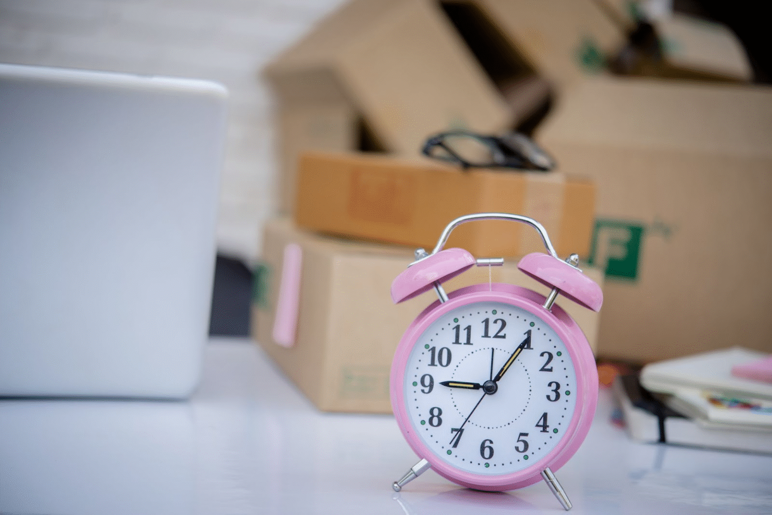 A pink alarm clock on a desk with moving boxes in the background, symbolizing time-saving packing tips for a stress-free move.