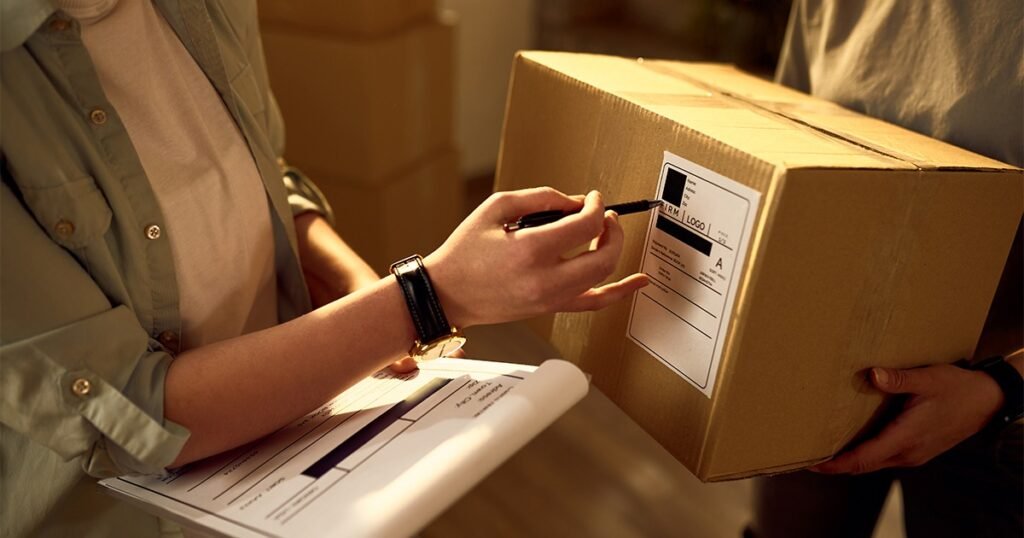 A man holds a pen and a box labeled "Label Boxes Clearly and Consistently" with a sheet of paper beside it.