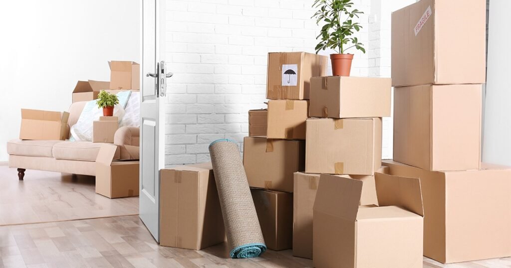 A room filled with stacked moving boxes, a couch, and a plant, emphasizing the importance of packing room by room.