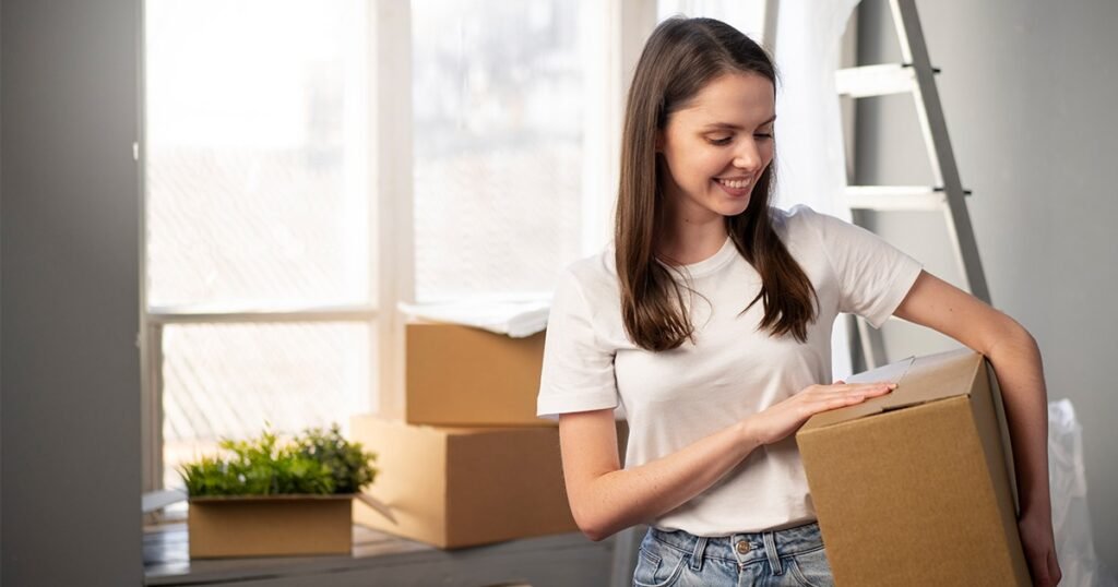 A cheerful woman with a box in hand, promoting the idea of keeping essentials for the first night.