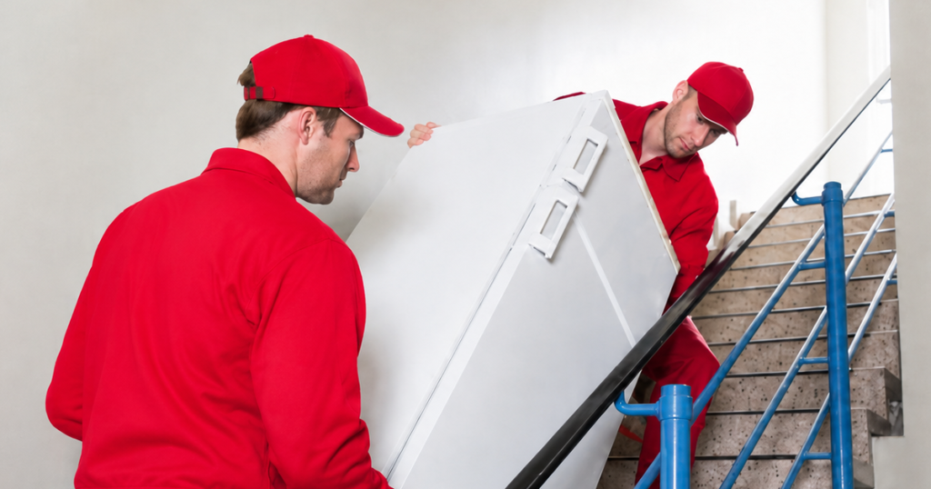 Two movers carrying a large white appliance upstairs.